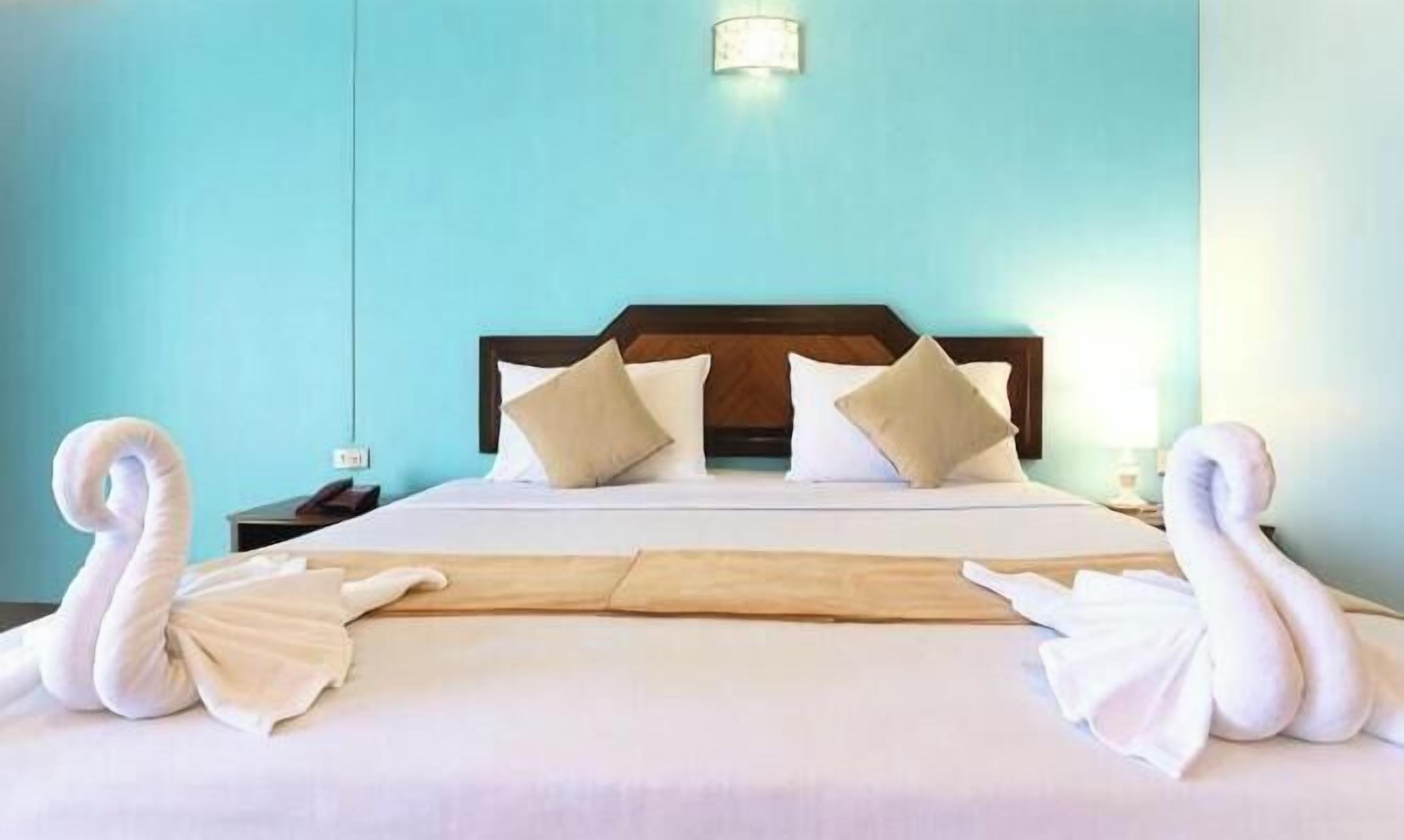 A hotel room with a bed, pillows, a nightstand, and a wall-mounted light fixture.