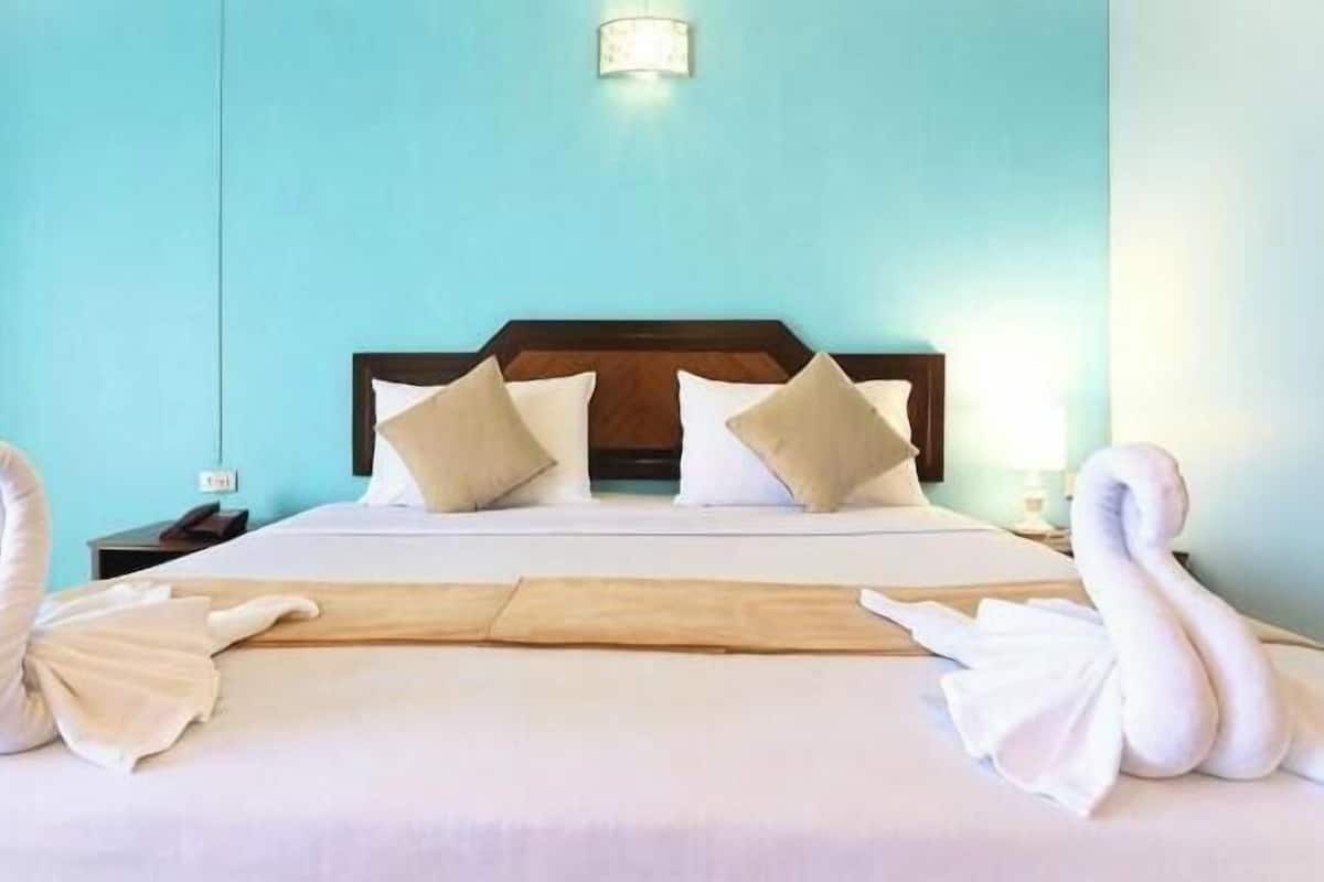 A hotel room with a bed, pillows, a nightstand, and a wall-mounted light fixture.