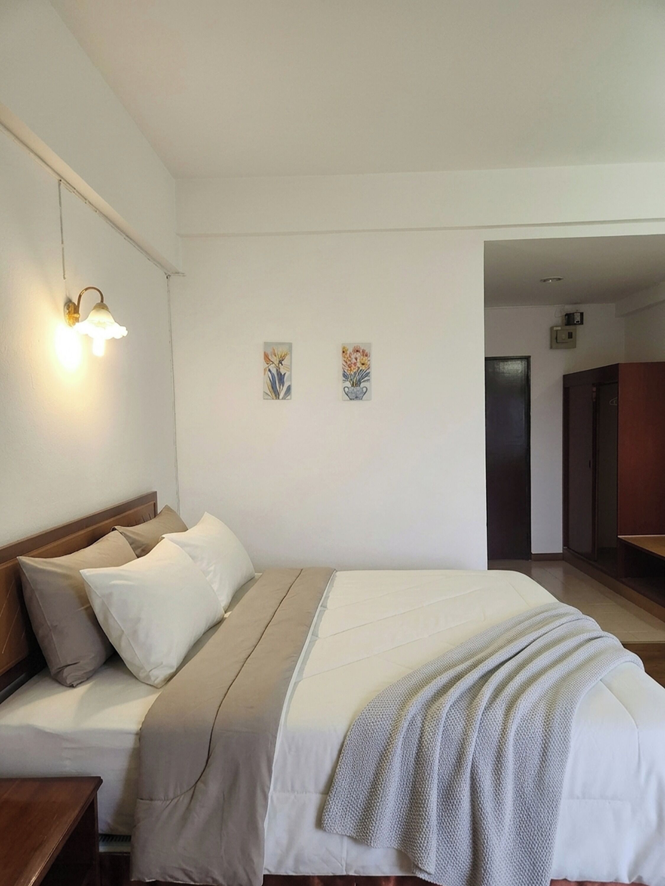 A bedroom with a bed, bedside tables, wall-mounted light, and two small wall art pieces.