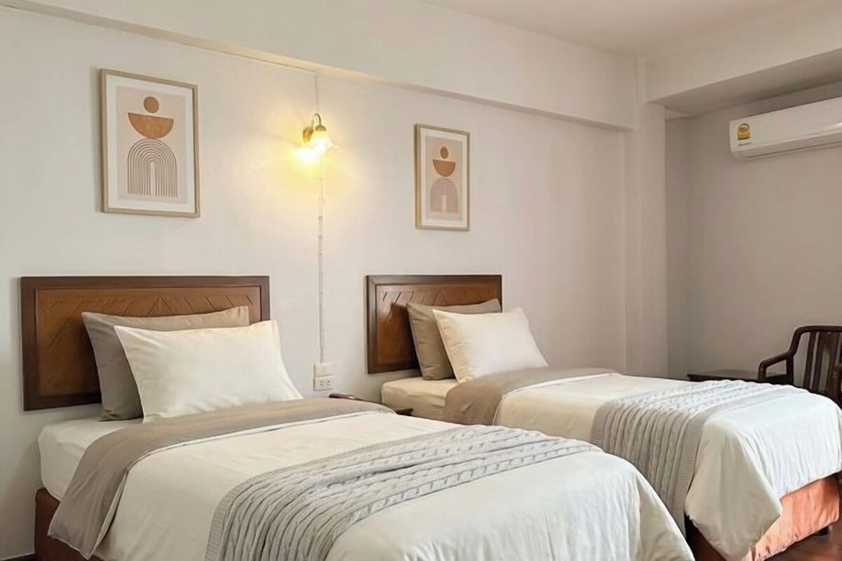 Une chambre d’hôtel avec deux lits, une table de chevet, une lampe fixée au mur et une chaise.