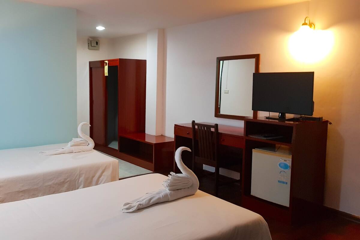 Ein Hotelzimmer mit zwei Betten, einem Schreibtisch, einem Stuhl, einem Fernseher und einem Spiegel.