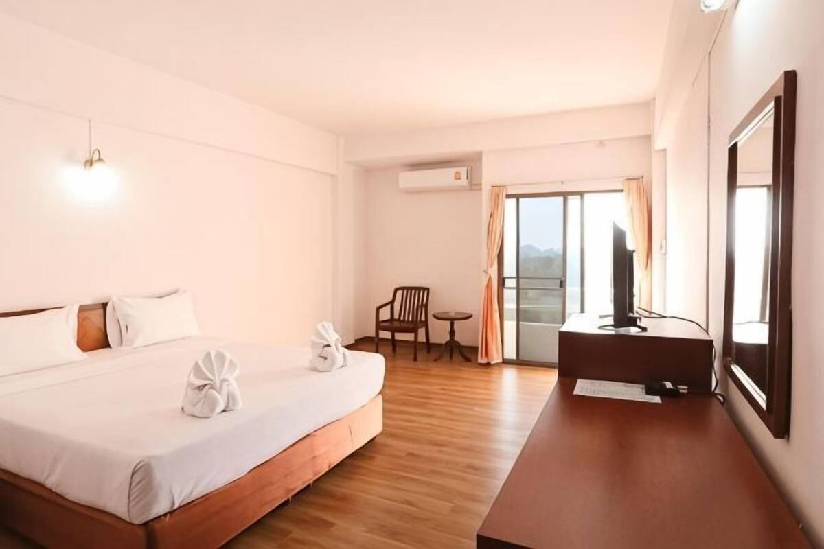 Ein Hotelzimmer mit Bett, Schreibtisch, Sessel, Fernseher und einem Balkon mit Vorhängen.