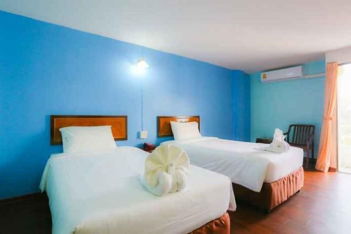 A hotel room with two beds, a blue wall, a wooden headboard, and a window with curtains.
