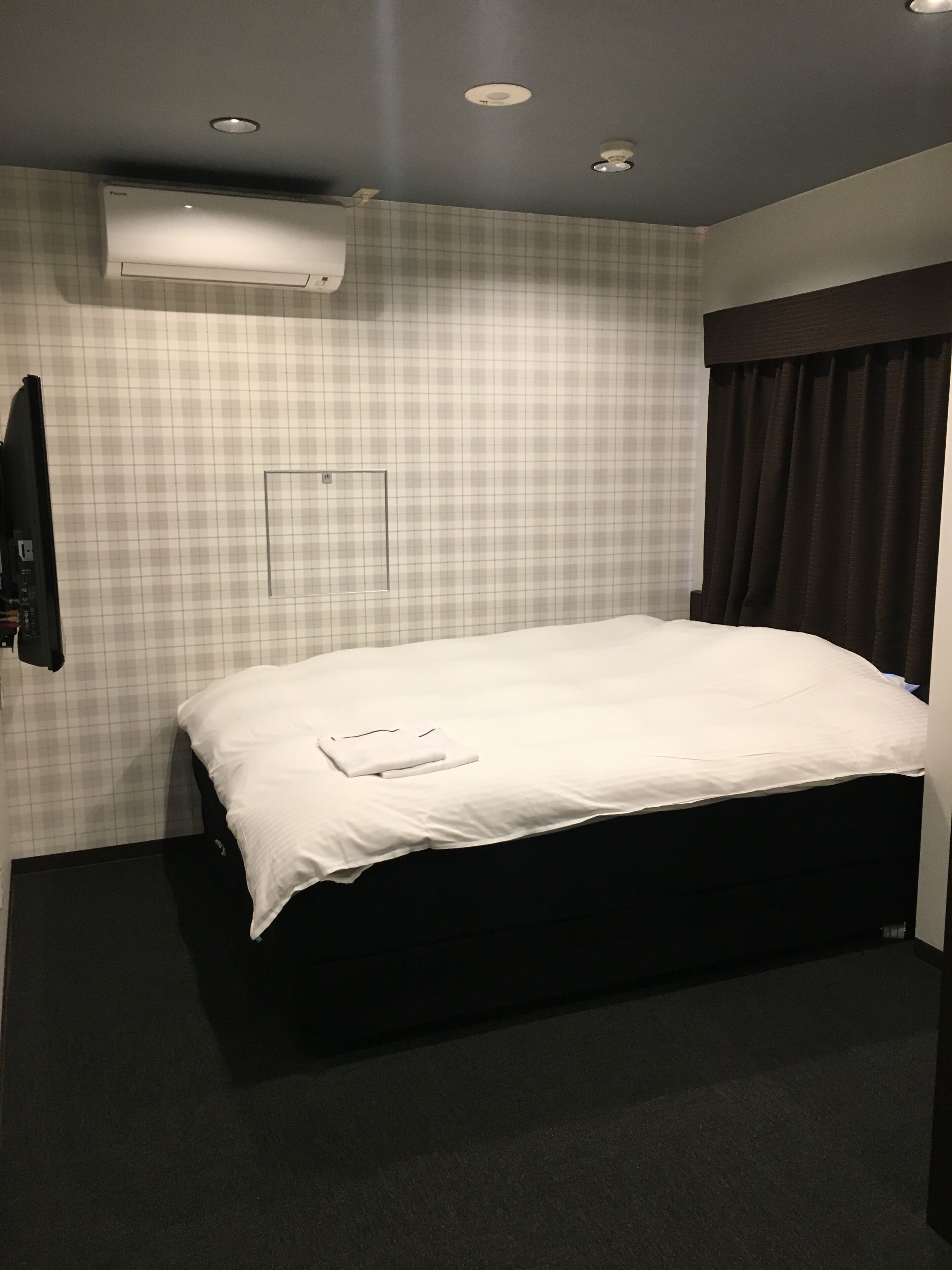 Quarto de hotel com cama grande, ar condicionado, cabeceira escura e padrão de parede xadrez.