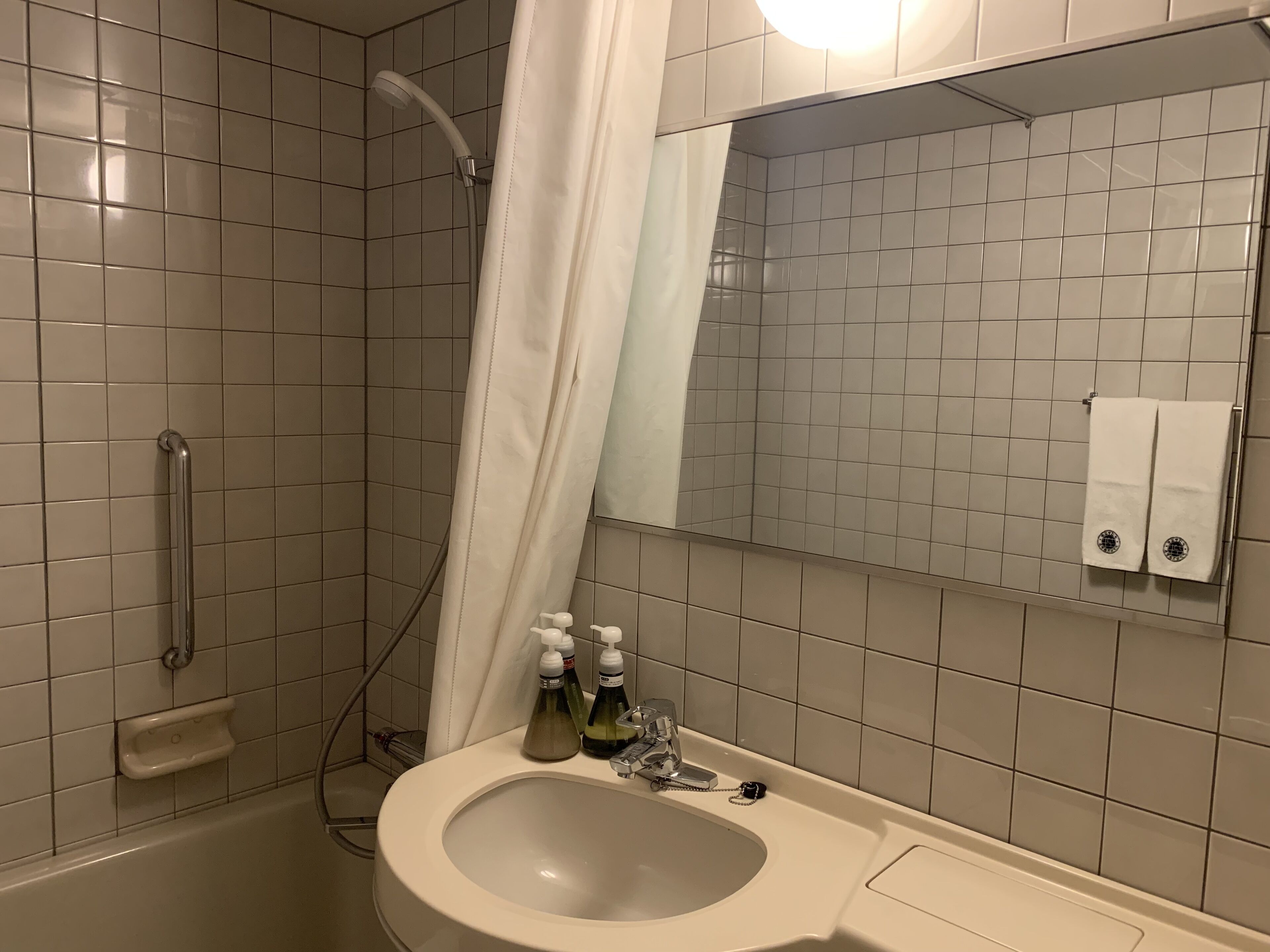 A bathroom with a shower, a sink with soap dispensers, and a towel rack.
