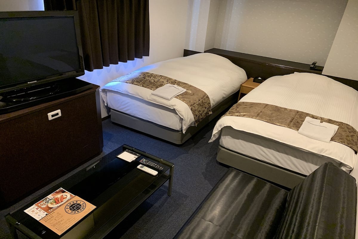 A hotel room with two beds, a TV, a desk with a menu, and a nightstand.
