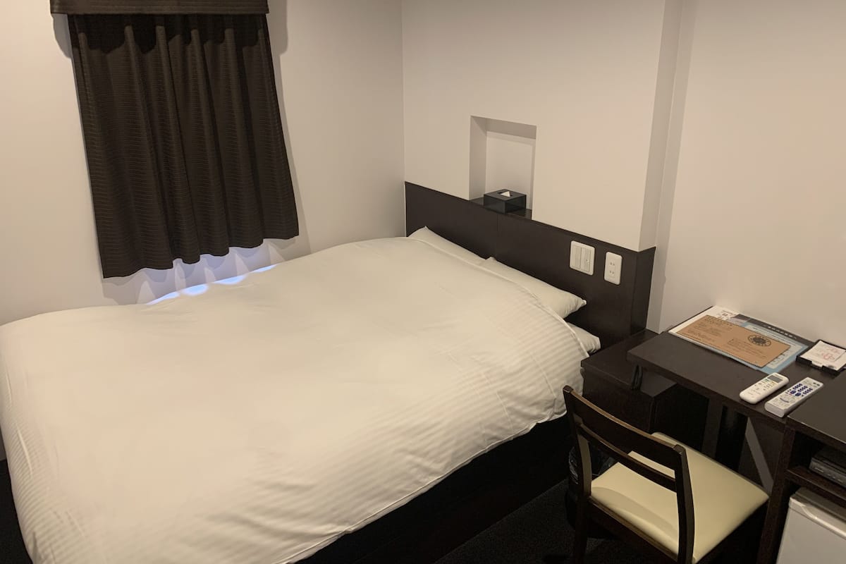A hotel room with a single bed, a desk with a chair, a small table, and a mirror.