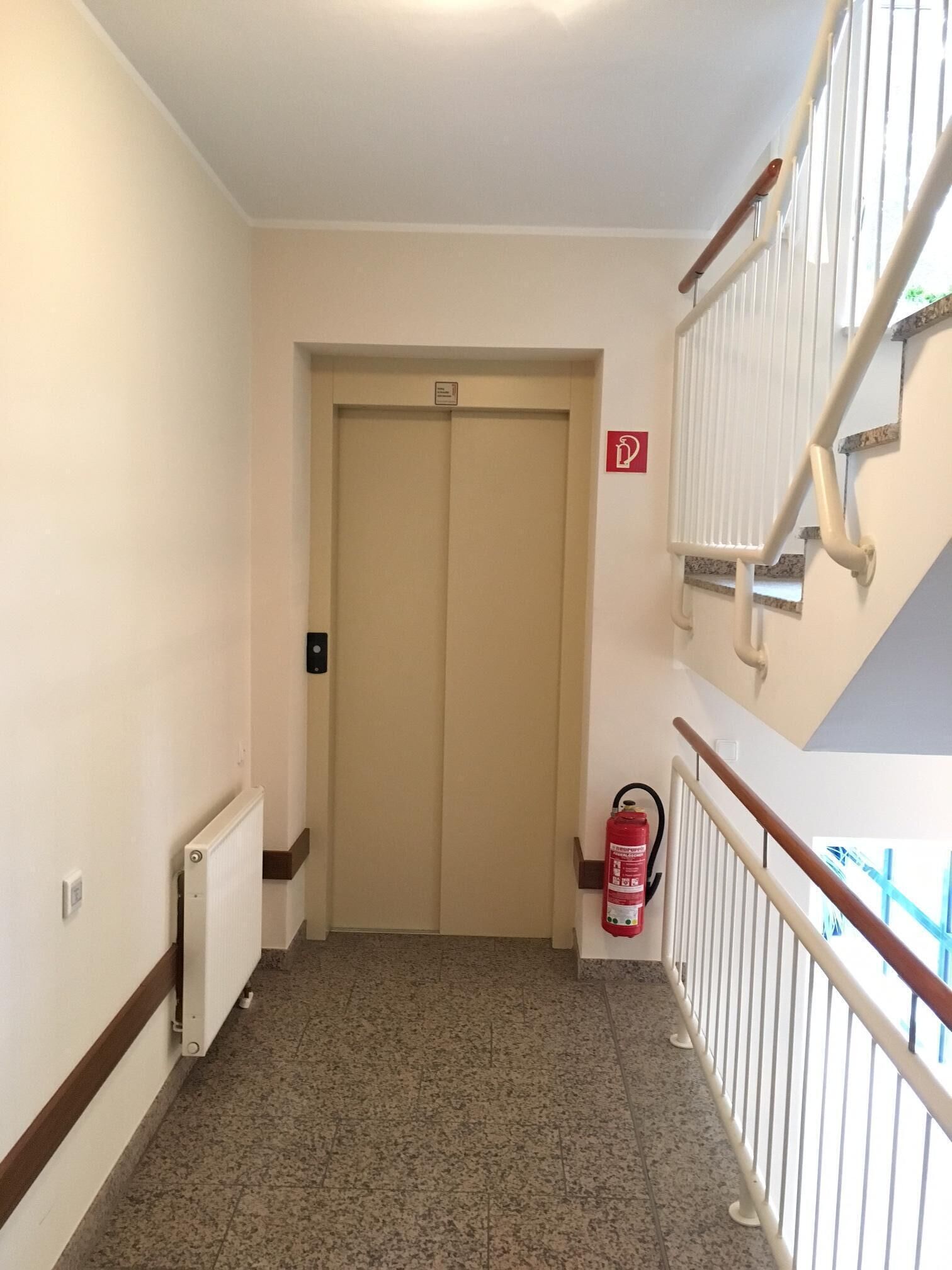Un corridoio con una porta chiusa, un estintore e un termosifone.