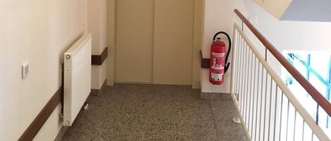 Un corridoio con una porta chiusa, un estintore e un termosifone.