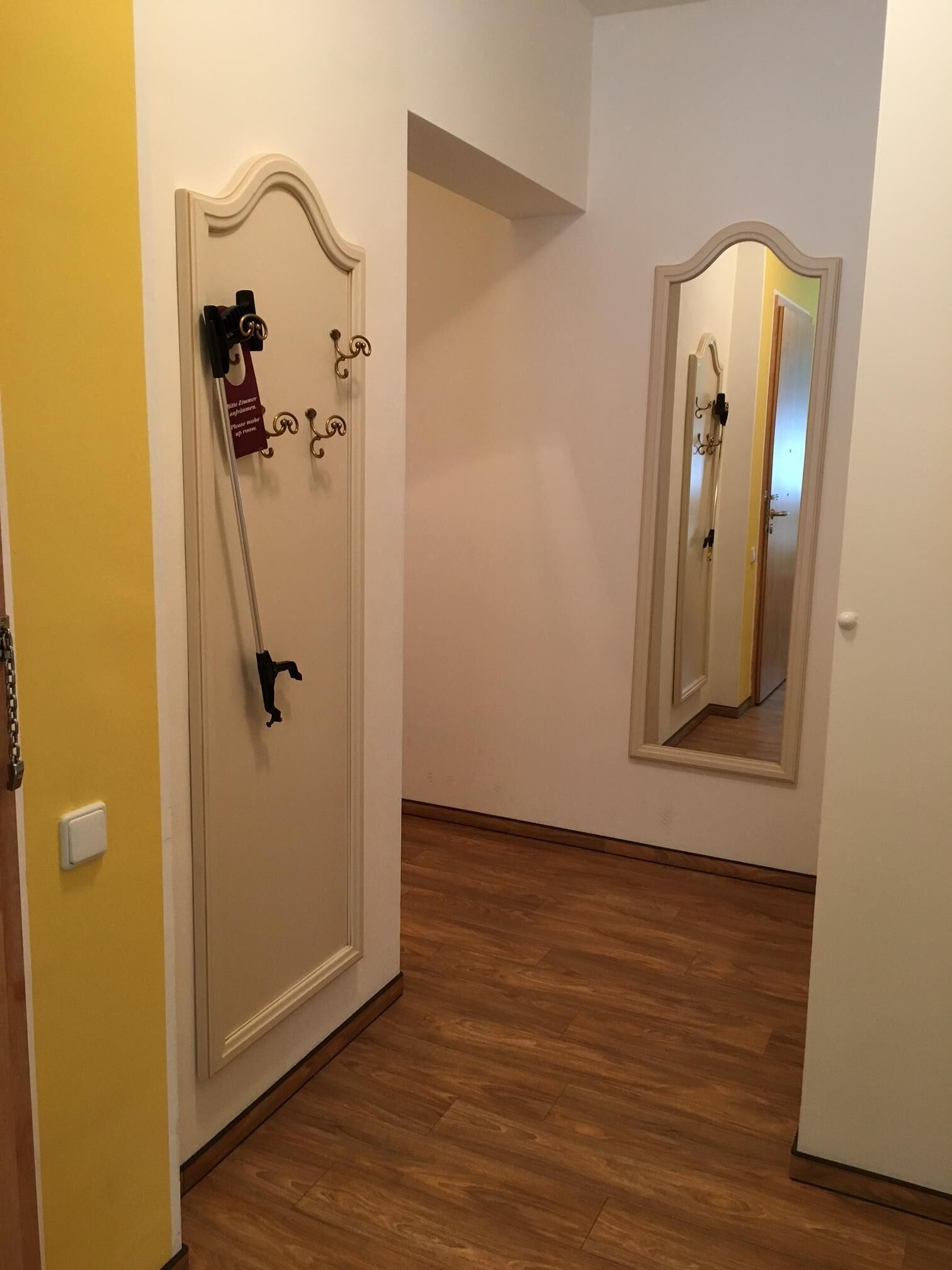 A hallway with a wooden floor, a door with a mirror, and a yellow wall.