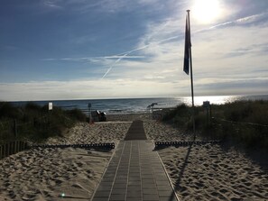 A beach pathway leading to the ocean with a flagpole and a signpost.