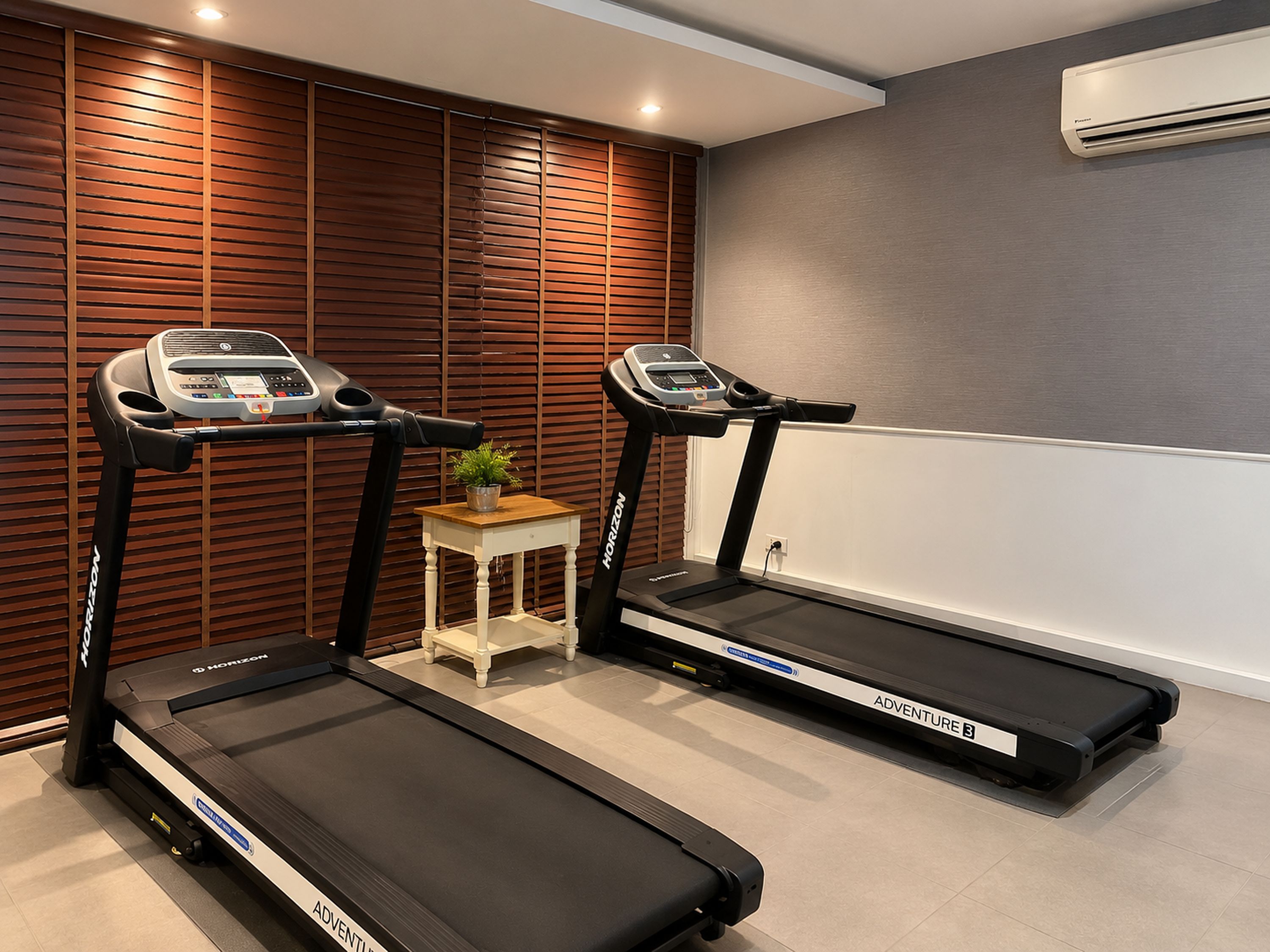A home gym with two treadmills, a small table with a plant, and a wall-mounted air conditioner.