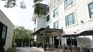 Un patio con mobiliario exterior, una zona cubierta y un edificio con amplios ventanales.