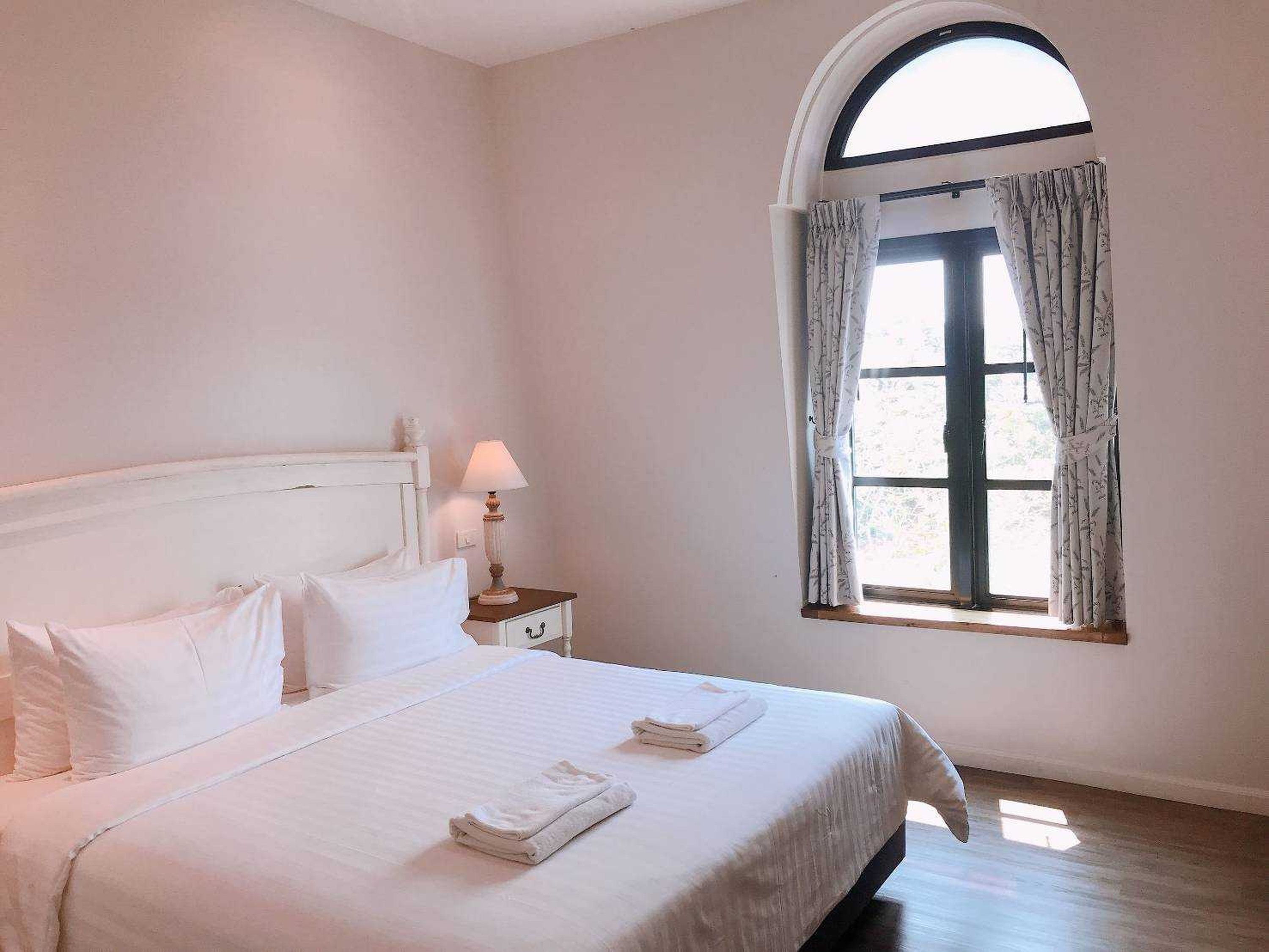 A bedroom with a bed, a nightstand, a lamp, and a window with curtains.