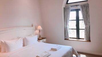 A bedroom with a bed, a nightstand, a lamp, and a window with curtains.