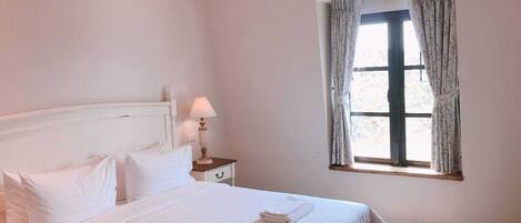 Une chambre à coucher avec un lit, une table de chevet, une lampe et une fenêtre avec des rideaux.