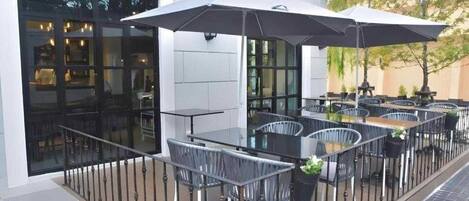 An outdoor patio with tables and chairs, a covered seating area, and a view of the interior through glass doors.