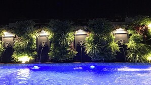 Zona de piscina nocturna con plantas iluminadas y un elemento acuático.