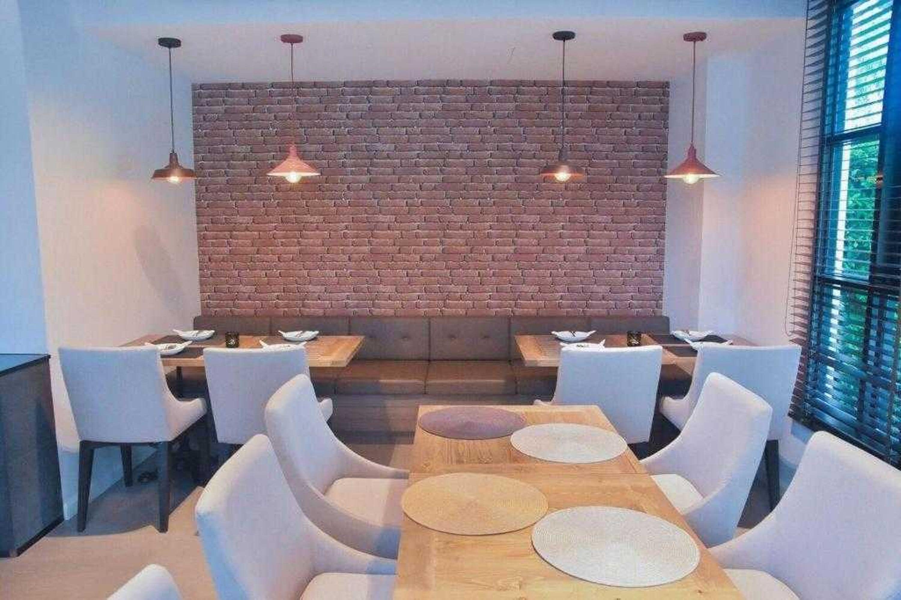 A modern dining area with a brick wall, white chairs, and pendant lights.