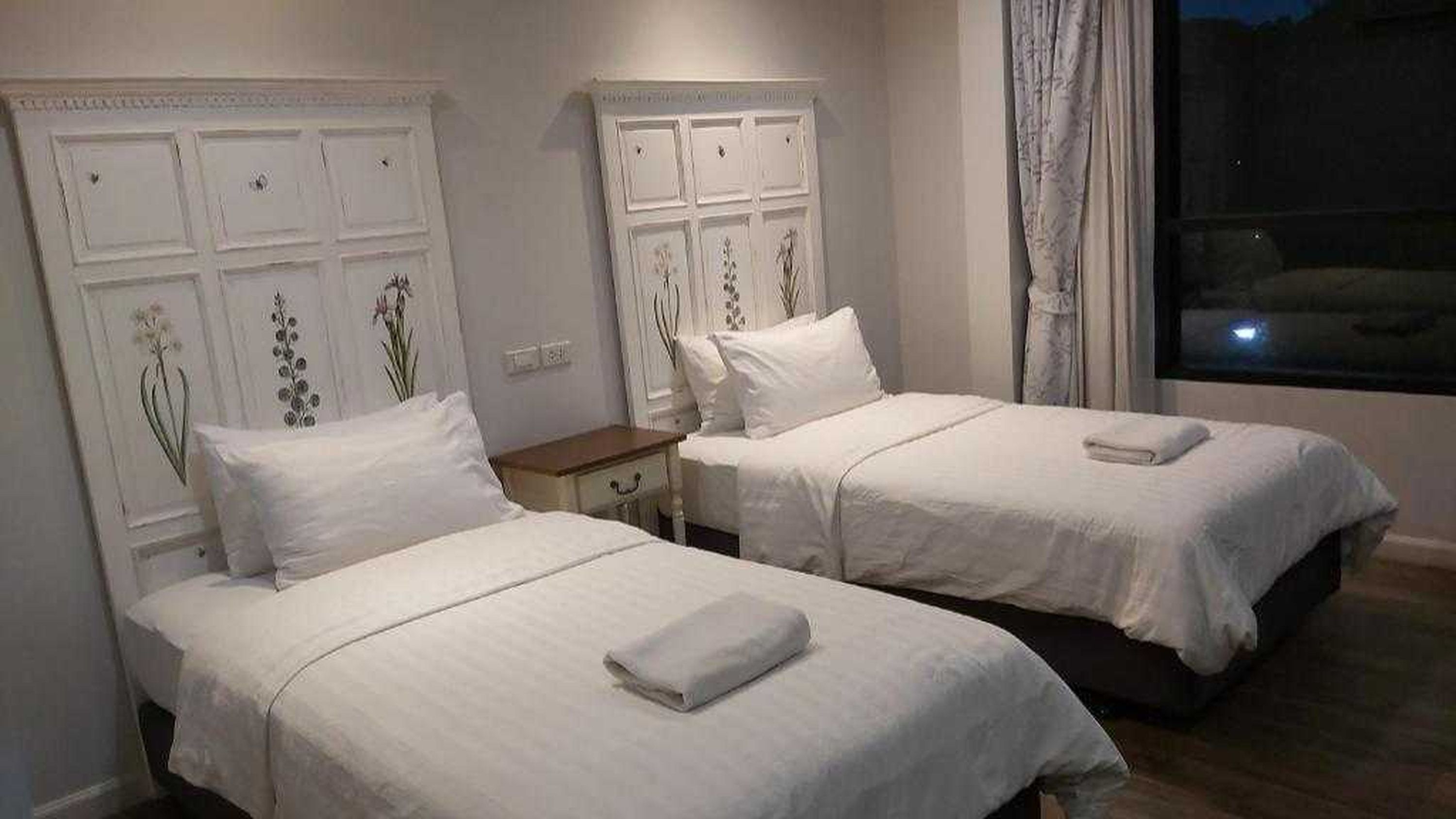 Une chambre d’hôtel avec deux lits, chacun recouvert d’une courtepointe blanche et agrémenté d’oreillers, une table de chevet et une fenêtre avec des rideaux.