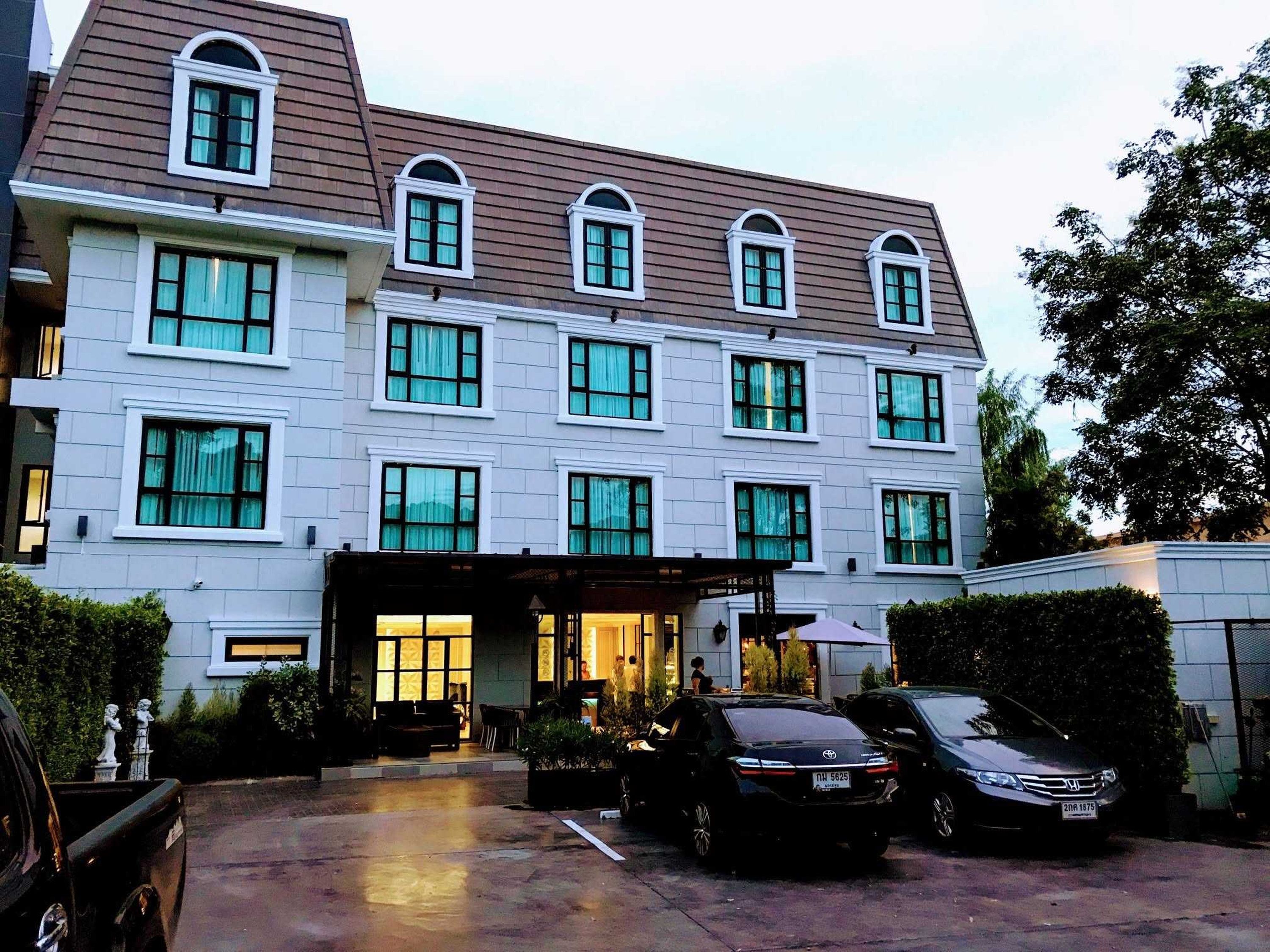 A multi-story hotel with a central entrance, a parking area, and a vehicle parked in front.