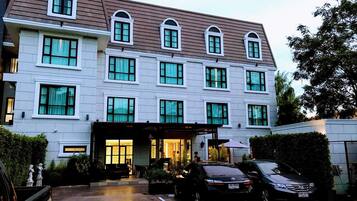 A multi-story hotel with a central entrance, a parking area, and a vehicle parked in front.