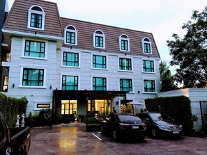 Un hotel de varios pisos con una entrada central, un área de estacionamiento y un vehículo estacionado al frente.