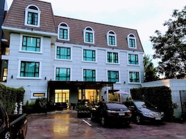 Un hotel de varios pisos con una entrada central, un área de estacionamiento y un vehículo estacionado al frente.