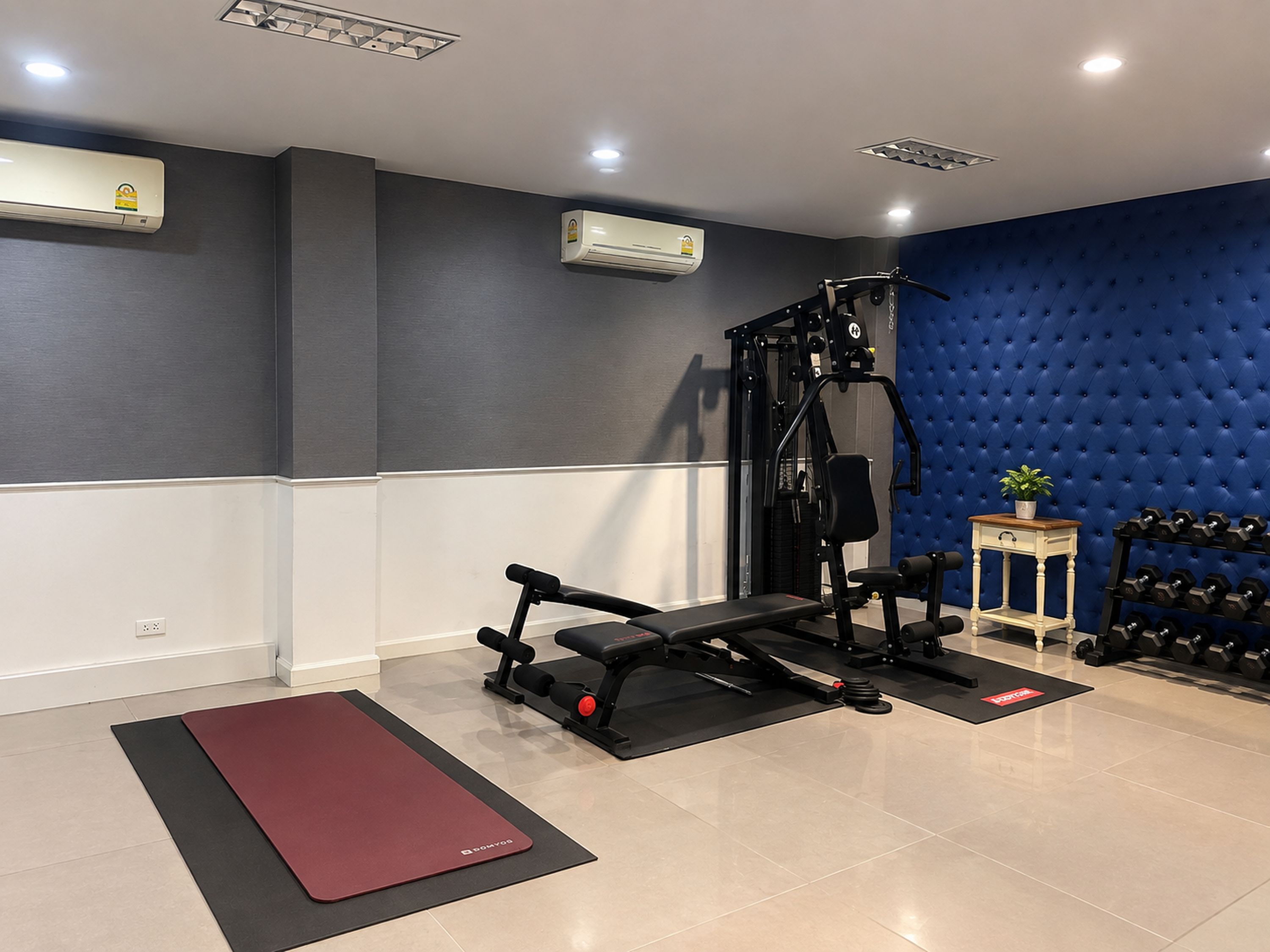 A gym with a bench press, dumbbells, and a blue wall.