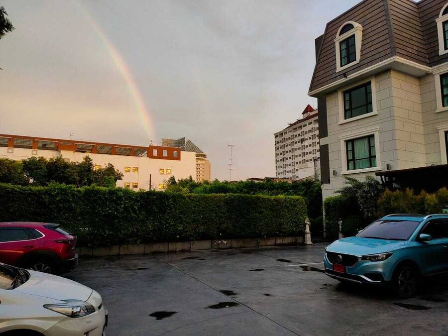 A parking lot with two cars, a building with a sloped roof, and a rainbow in the sky.