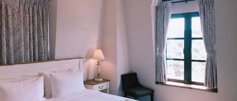 A hotel room with a bed, a nightstand, a lamp, a chair, and a window with curtains.