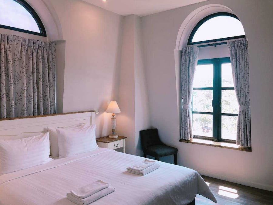 A hotel room with a bed, a nightstand, a lamp, a chair, and a window with curtains.