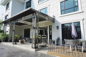 Entrada de hotel con zona exterior techada, disposición de asientos y acceso mediante portón.