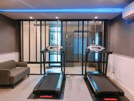 Un gimnasio con dos cintas de correr, un sofá gris y una ventana con persianas.