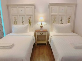 Una habitación de hotel con dos camas individuales, una mesita de noche con lámpara y decoración floral en las paredes.