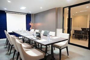 A conference room with a long table, chairs, a projector screen, and a laptop. - Palette Marquise Boutique Hotel (Rayong)