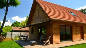 Une cabane en bois avec un toit recouvert de tuiles rouges, une terrasse avec des meubles d’extérieur et une porte-fenêtre coulissante.