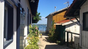 Une ruelle étroite bordée de bâtiments des deux côtés, un ciel bleu dégagé et une vue sur des bateaux au loin.