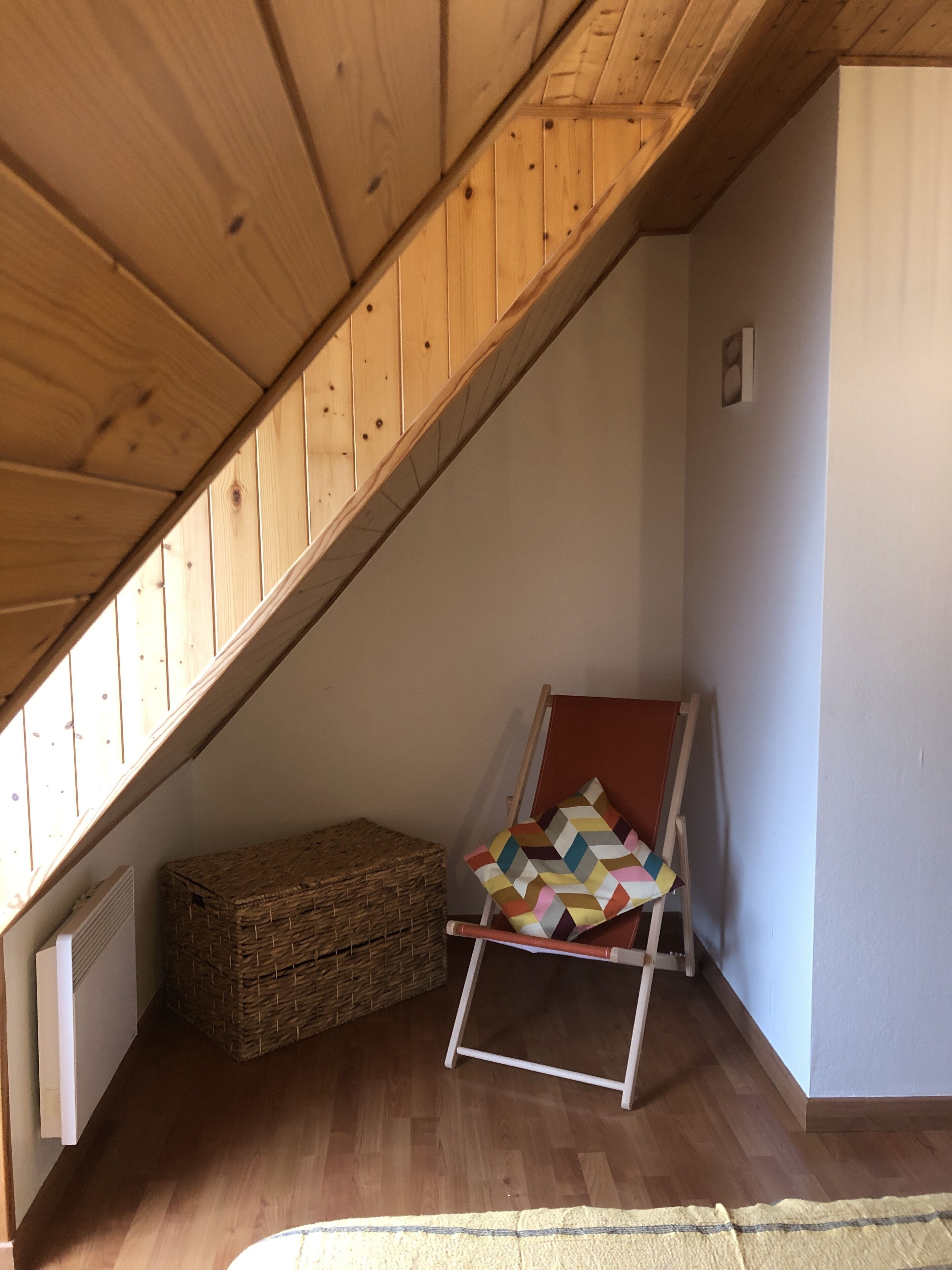 A corner room with a sloped ceiling, a wicker basket, a colorful chair, and a radiator.