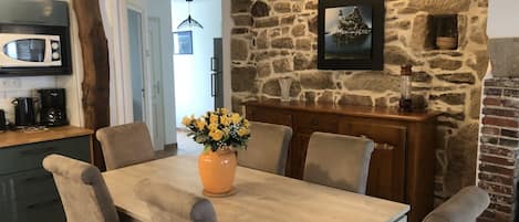 A dining area with a stone wall, a framed picture, and a vase of flowers on the table.
