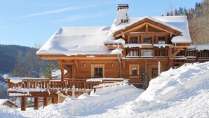 Une cabane en rondins de bois, avec un toit enneigé et une terrasse en bois.