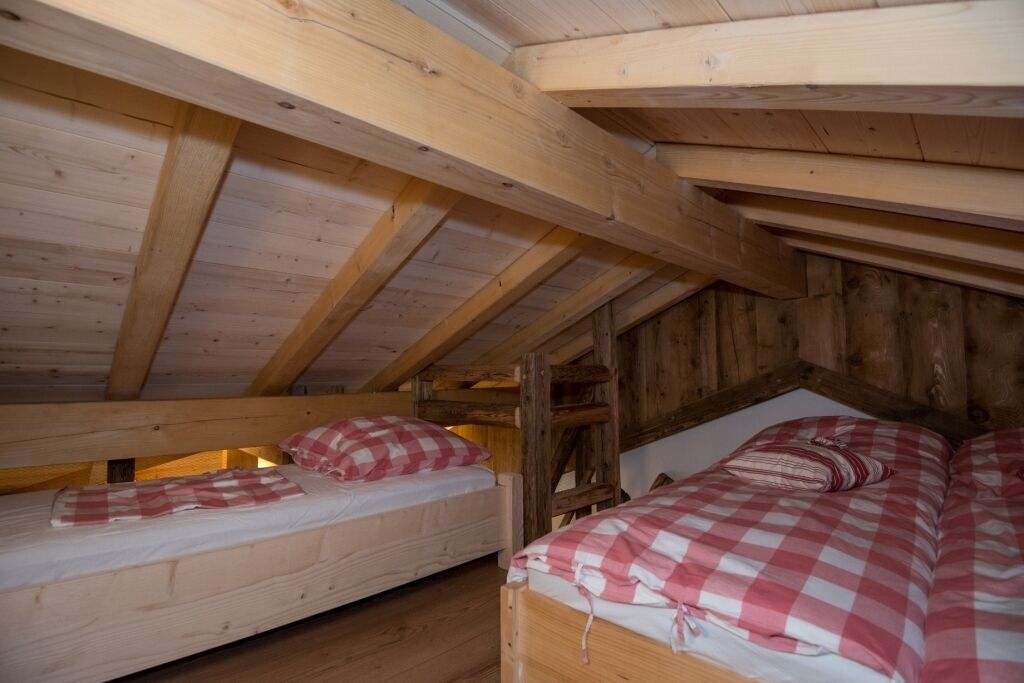 A wooden attic bedroom with two bunk beds, each with a checkered bedspread.