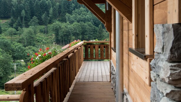 Une terrasse en bois avec un mur en pierre, entourée d’un paysage boisé.