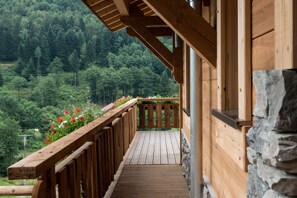 Une terrasse en bois avec un mur en pierre, entourée d’un paysage boisé.