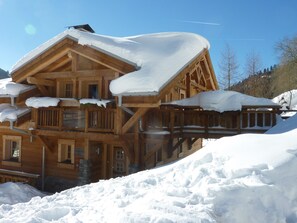 Een houten chalet met meerdere балконы, bedekt met sneeuw, gelegen in een besneeuwd landschap.