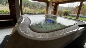 Un bain à remous avec un intérieur en bois et une vue sur un paysage boisé.