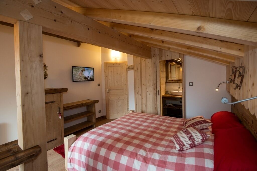 Een slaapkamer met een geruit beddegoed, houten balken, een houten bankje en een televisie aan de muur.
