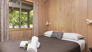 A wooden-paneled room with a bed, curtains, and a window with a view of trees.