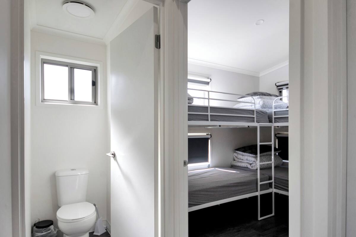 A compact, single-room accommodation with a bunk bed, a toilet, and a window.
