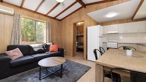 Un espacio habitable compacto con sofá, una mesita de centro y una zona de comedor con sillas. Se observa una cocina en el fondo, con alacenas blancas y un refrigerador.